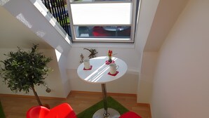 Een kleine kamer met een ronde tafel, twee rode stoelen, een bloempot en een raam.