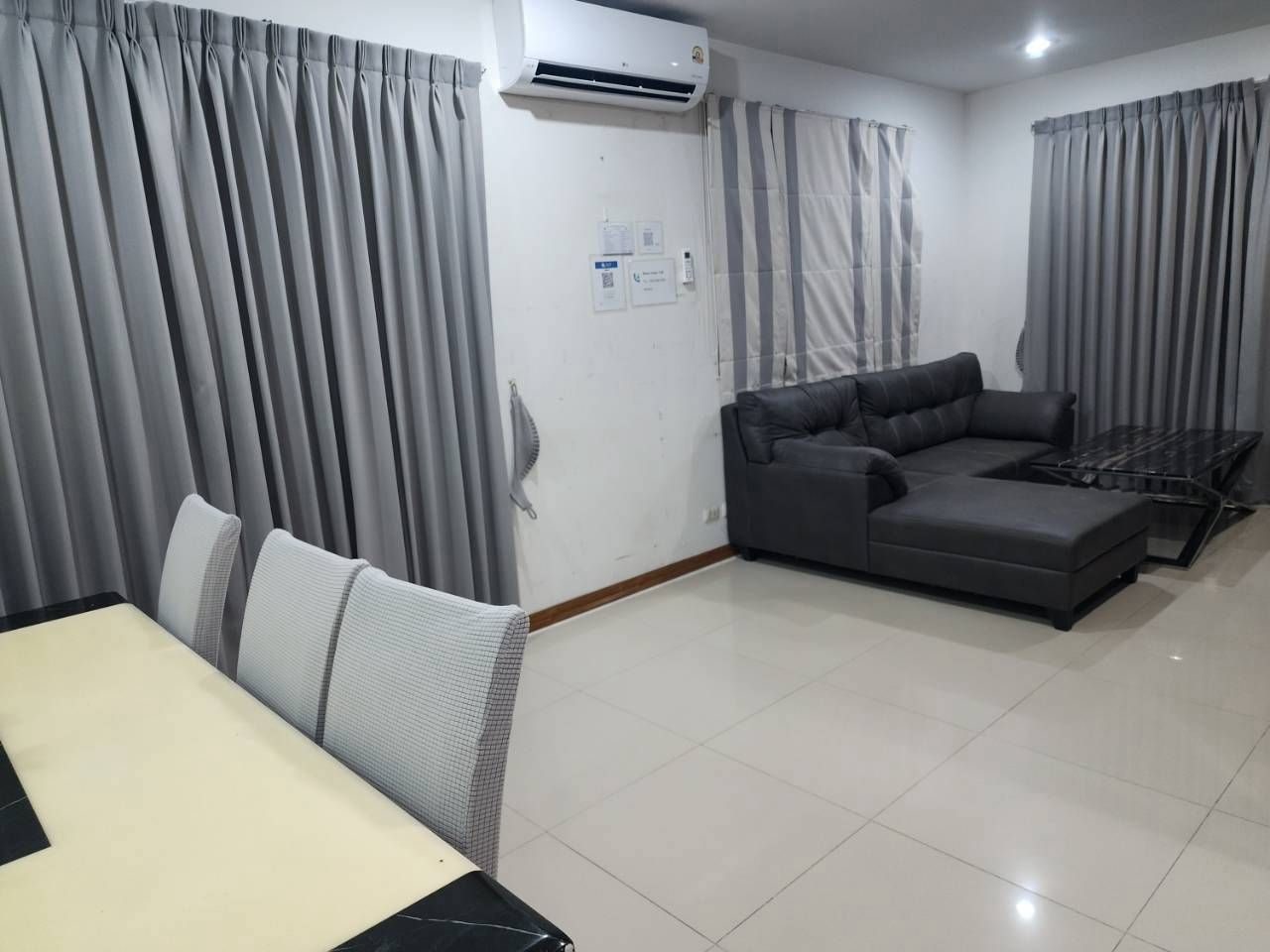 Una sala moderna con un sofá modular, una mesa de comedor con sillas y cortinas grises.