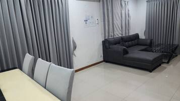 Una sala moderna con un sofá modular, una mesa de comedor con sillas y cortinas grises.
