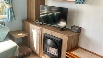 A compact room with a television, a fireplace, a small table, and a bed.