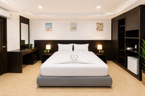 A hotel room with a large bed, two bedside tables with lamps, a wardrobe, and a small refrigerator. - Charming Guest Room in Central Pa Tong, Thailand (Pa Tong)