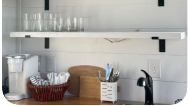 Une cuisine avec des étagères blanches où sont rangés des verres à vin et un appareil à café.
