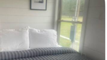 A bedroom with a bed, white pillows, and a window with a view of greenery.