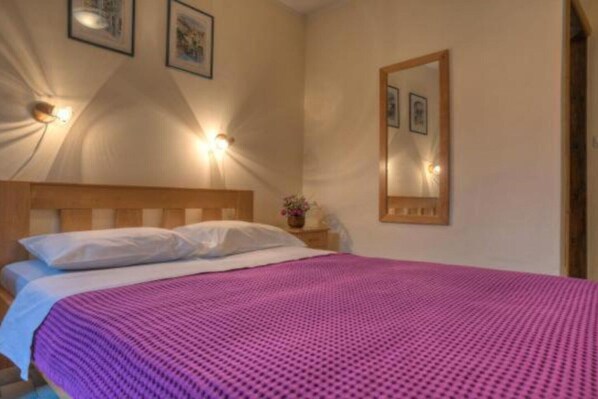 Ein Schlafzimmer mit einem hölzernen Kopfteil, einer pinkfarbenen Bettdecke, zwei weißen Kissen, einem Nachttisch mit Lampe und einem Spiegel an der Wand.