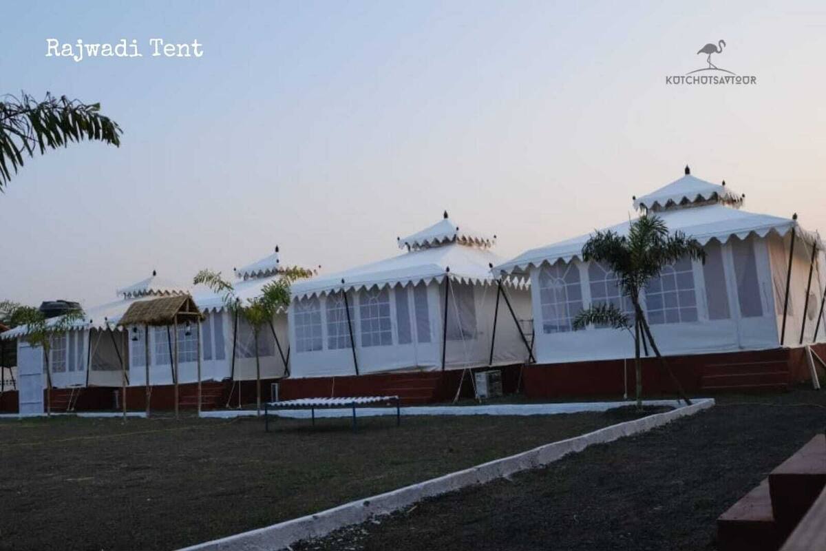 A series of white tents with peaked roofs, arranged in a row, with a grassy area in the foreground and a clear sky in the background.