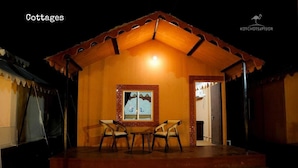 Una cabaña acogedora con techo de tejas, una obra de arte enmarcada sobre la puerta, y una pequeña mesa con sillas en el centro.