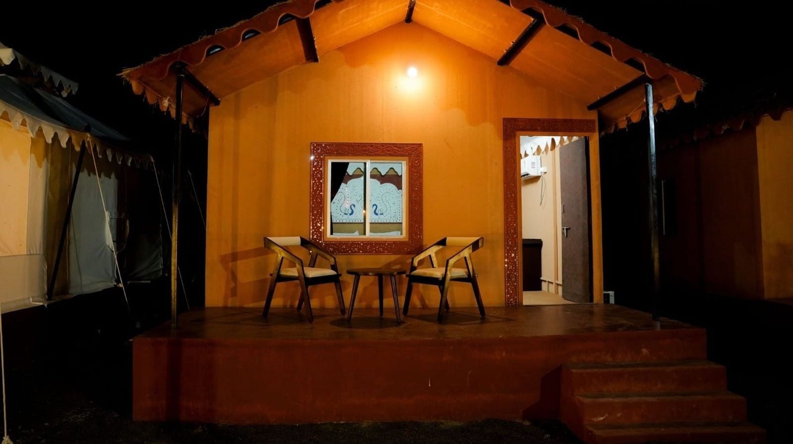 A cozy cottage with a tiled roof, a framed artwork above the door, and a small table and chairs in the center.