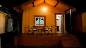 A cozy cottage with a tiled roof, a framed artwork above the door, and a small table and chairs in the center. - The Desert Resort (Bhuj)