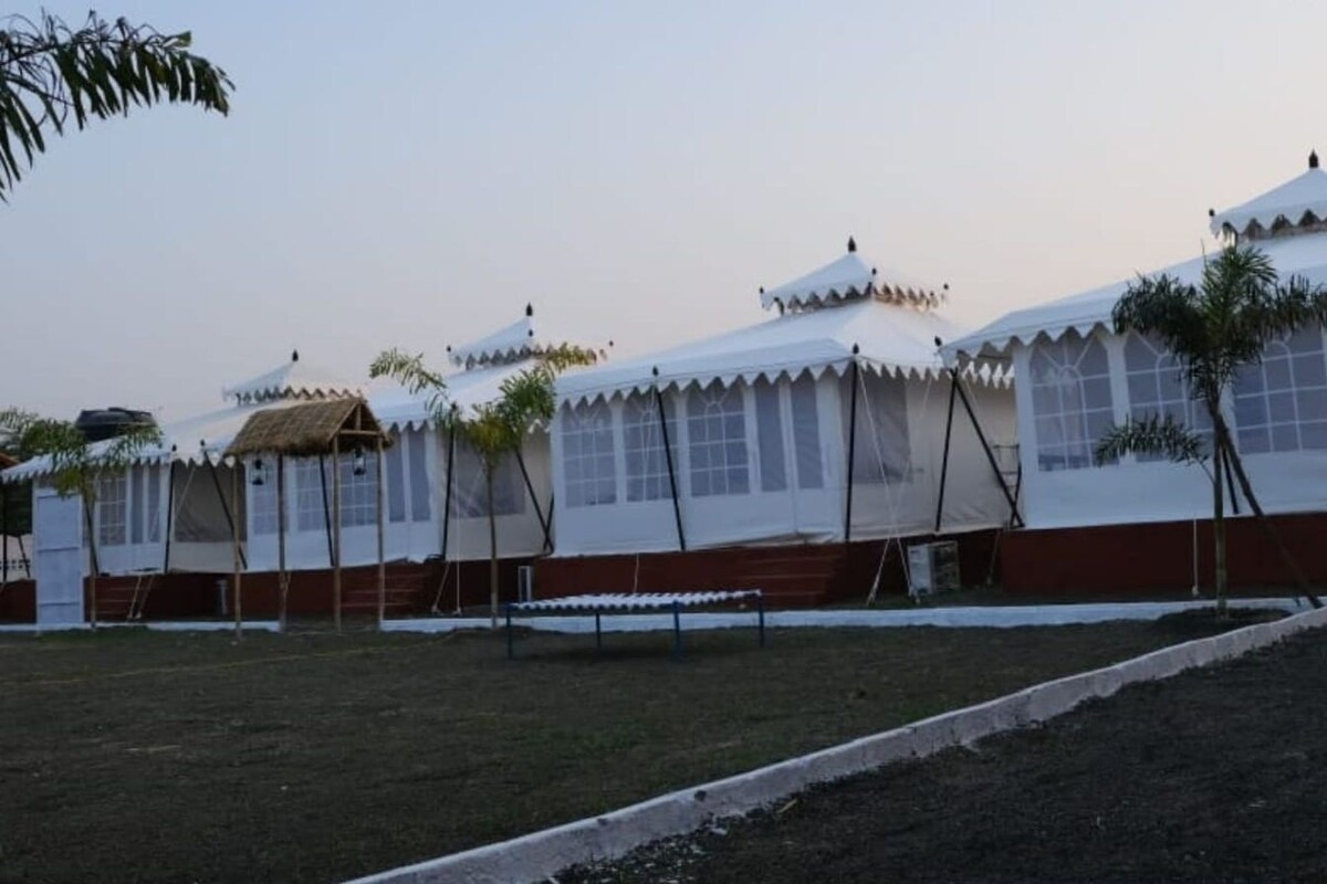 A series of white tents with peaked roofs, arranged in a row, with a grassy area in the foreground and a clear sky in the background.