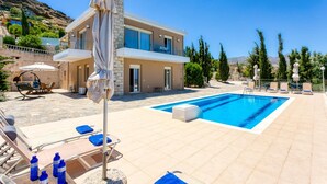 A modern two-story house with a swimming pool, outdoor seating, and a view of the surrounding landscape.