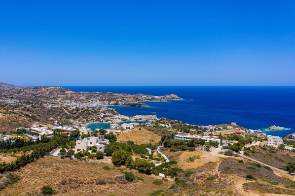 A coastal town with buildings along the shoreline, a clear blue sky, and a view of the sea.
