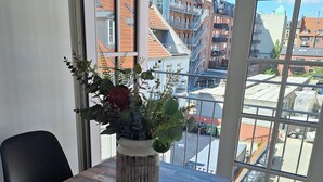 Una habitación con un ventanal grande, una mesa de madera, dos sillas negras y una planta en maceta.