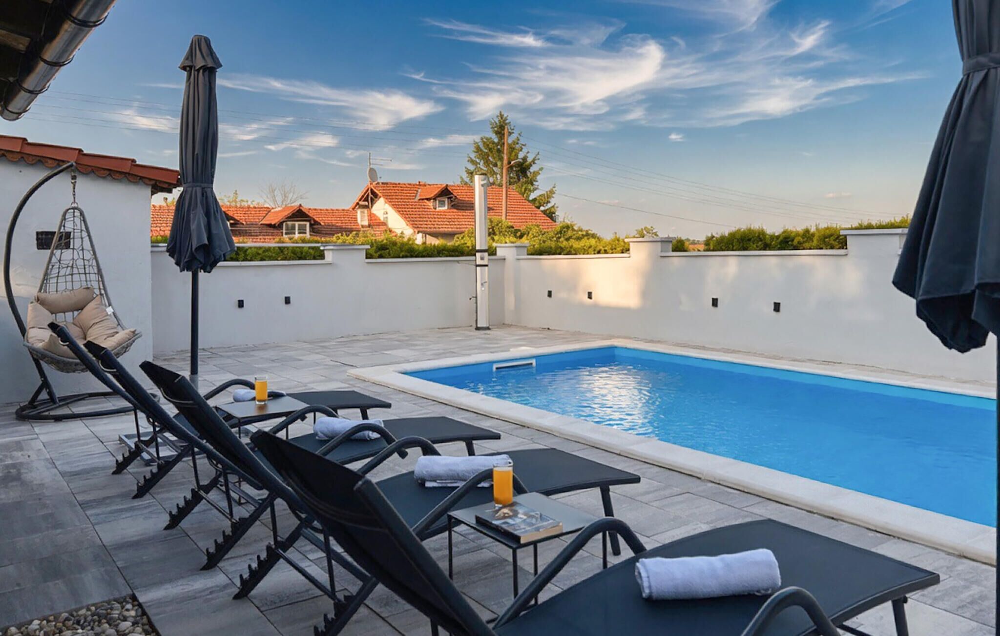 A rooftop pool area with lounge chairs, a hanging chair, and a table with a drink.