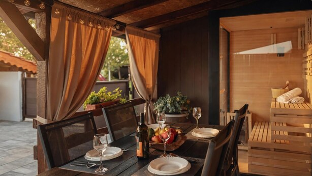 An outdoor dining area with wooden furniture, a table set with plates, glasses, and a bottle.
