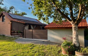 A house with a solar panel roof, a fenced yard, and a tree.