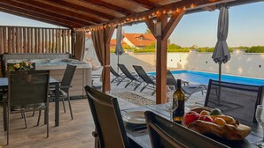 A covered outdoor dining area with a pool, lounge chairs, and a hot tub.