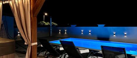 An outdoor pool area with lounge chairs and string lights.