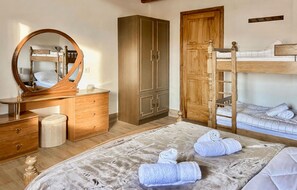 A bedroom with a bunk bed, a wooden wardrobe, a vanity with a mirror, and a bedside table.