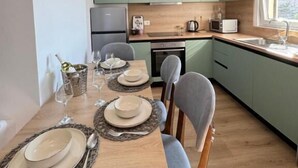A modern kitchen with green cabinets, a wooden dining table set for four, and a window providing natural light. - Apartment in City Center (Shkodër)