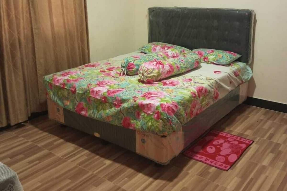 Una cama individual con ropa de cama floral, cabecera y un tapete rojo sobre piso de madera.