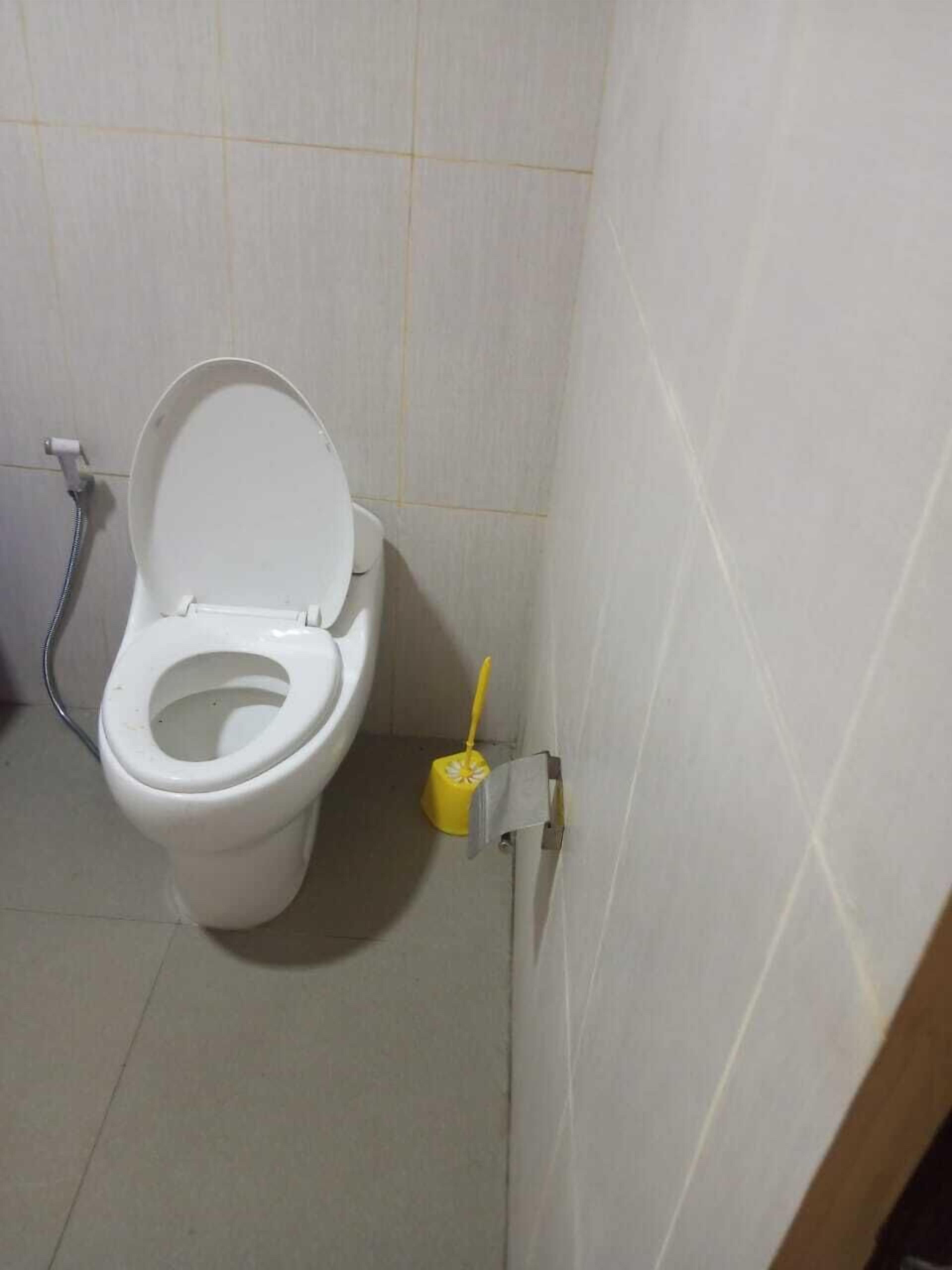 A white toilet with a closed lid, a yellow bidet spray, and a wall-mounted flush handle.