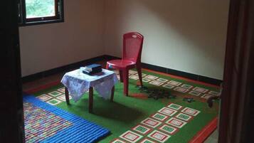 Una habitación pequeña con una silla de plástico roja, una mesita con mantel de encaje y una alfombra estampada.