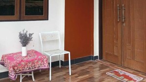 A room with a wooden floor, a white chair, a table with a red tablecloth, and a large wooden door. - Gloria Guest House (Ambon)