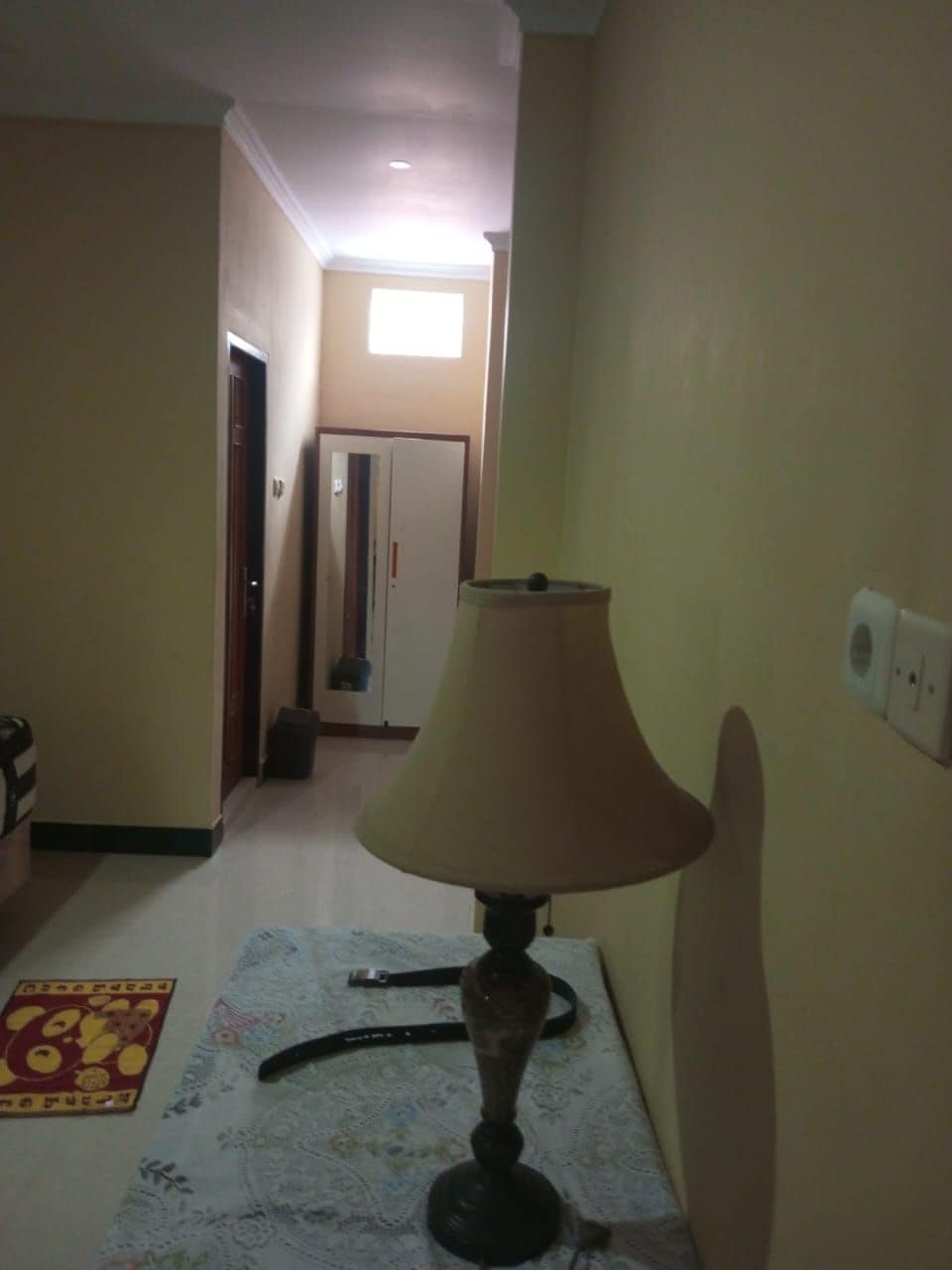 Un couloir avec une lampe sur une table, un tapis à motifs et une porte donnant sur une autre pièce.