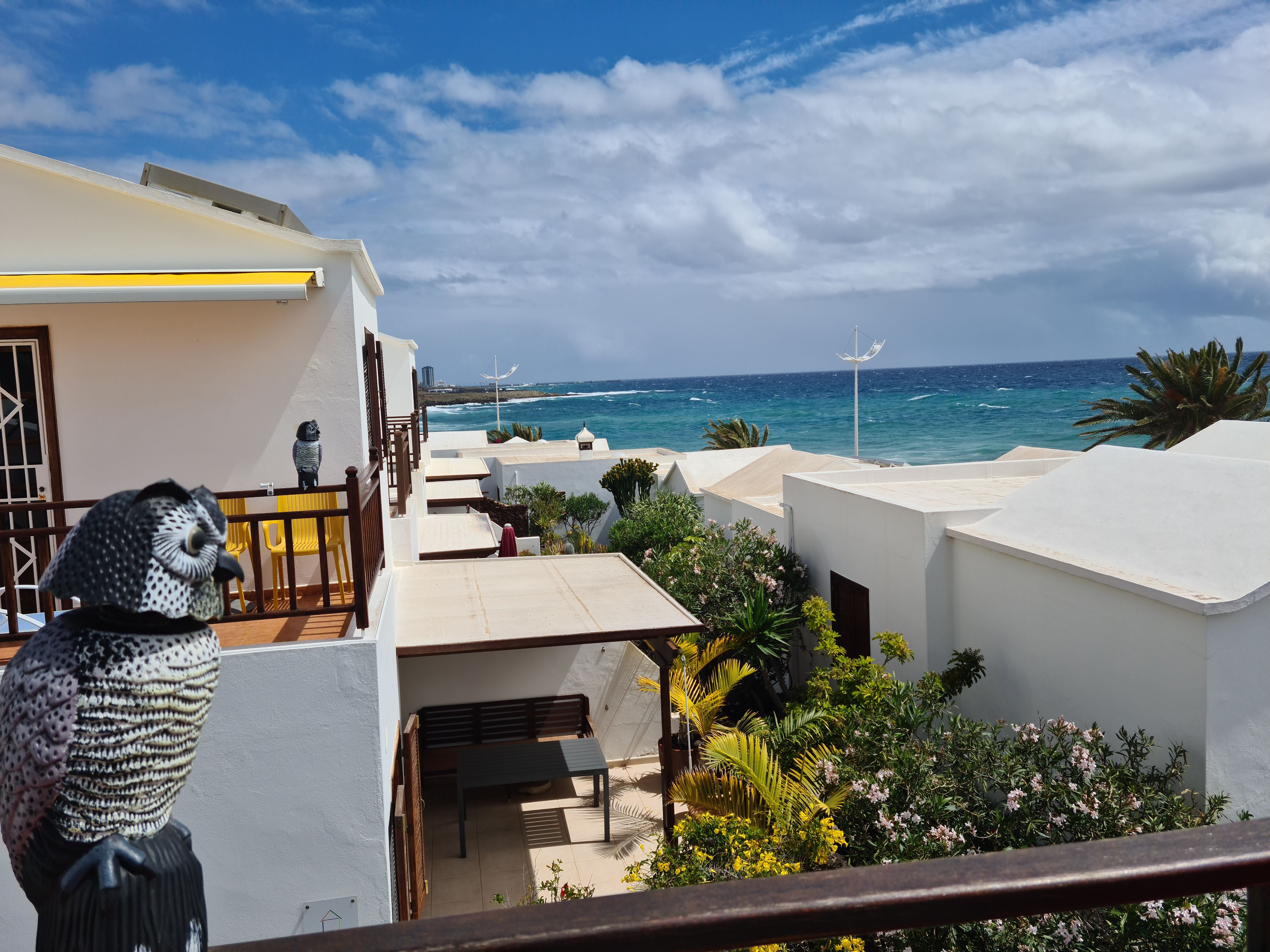A coastal property with a balcony overlooking the sea, a statue, and a patio area.
