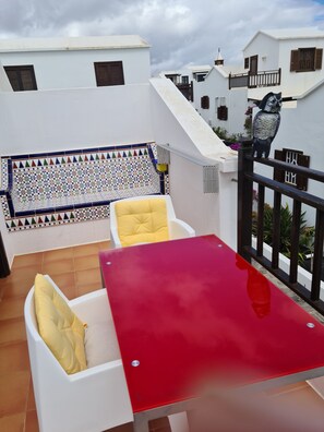Eine Terrasse mit einem roten Tisch und weißen Stühlen, einer dekorativen Fliesenwand und einer Katzenstatue.