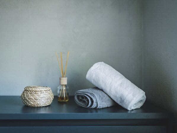 A shelf with a woven basket, a rolled towel, and a bottle with reed sticks. - Appartements Ager by we rent (Rauris)