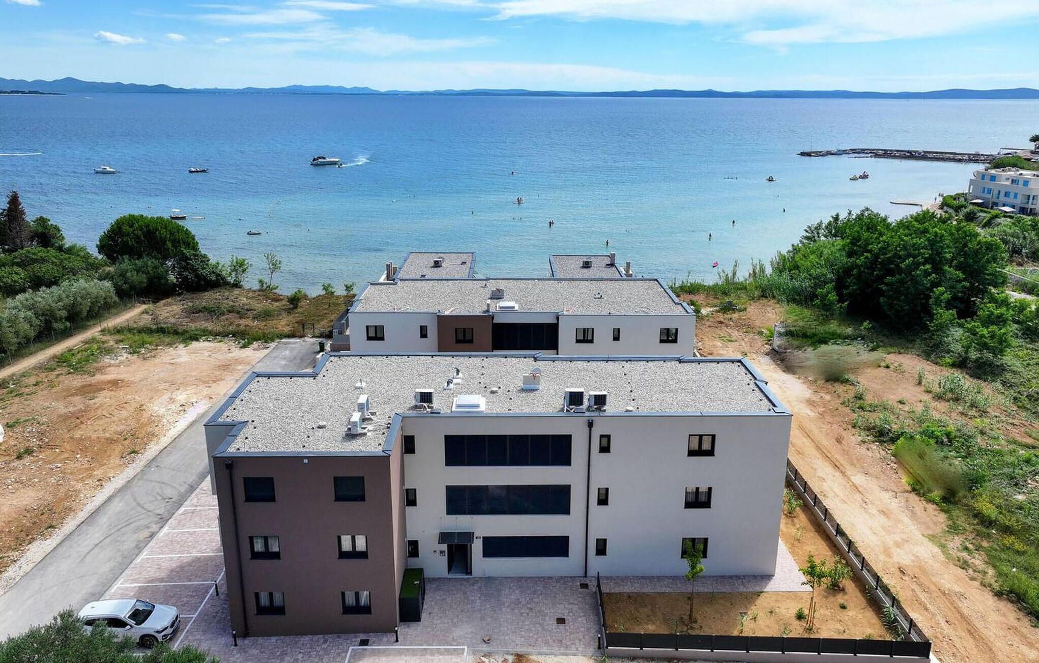 Un edificio moderno de varios pisos, con estacionamiento y vistas al mar con barcos.