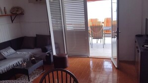 A living room with a sofa, a coffee table, and a chair. There is a sliding glass door leading to an outdoor area with chairs. - Two Bedroom Apartment With Terrace And Sea View (Vela Luka)