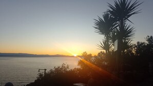 A sunset view over a body of water with a palm tree and a table with a person. - Two Bedroom Apartment With Terrace And Sea View (Vela Luka)