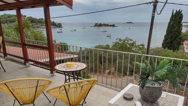 A balcony with wicker chairs and a table, overlooking a calm sea with boats and a small island. - Two Bedroom Apartment With Terrace And Sea View (Vela Luka)