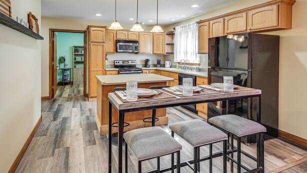 A modern kitchen with wooden cabinets, a central island with bar stools, a refrigerator, and a microwave. - 1 Mi to Main St! Family Farmhouse in West Unity (West Unity)