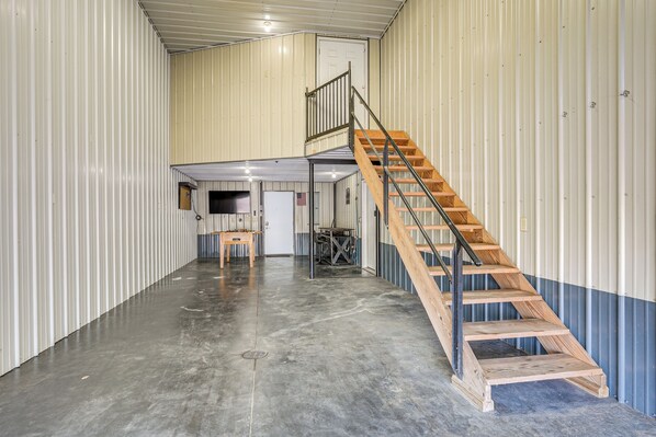 A spacious industrial-style interior with a central staircase and a door leading to a smaller enclosed area.
