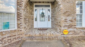 Un bâtiment en briques avec une porte blanche, un paillasson et un panneau d’avertissement de sécurité.