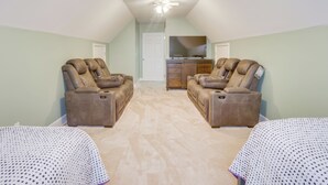 Une pièce avec deux fauteuils inclinables, un ventilateur de plafond et un téléviseur posé sur une commode en bois.
