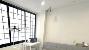 A room with a large window, a white sofa, a small table with a kettle, and a drying rack. - ORIGAMI Stay Osaka (Osaka)