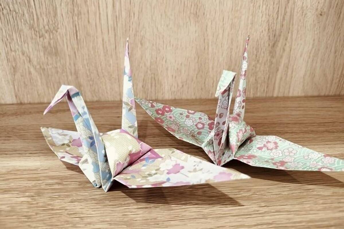 Two origami cranes on a wooden surface.