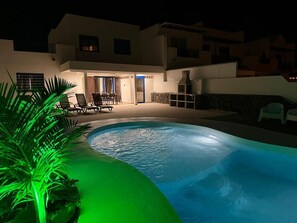 Una piscina con zona de patio, una mesa de comedor y sillas.
