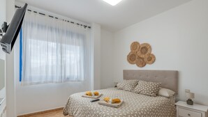 A bedroom with a bed, a nightstand, a wall-mounted lamp, a ceiling fan, and a window with sheer curtains. - Holiday Home 'Oasis 138' with Mountain View, Private Pool and Wi-Fi (Playa Blanca)