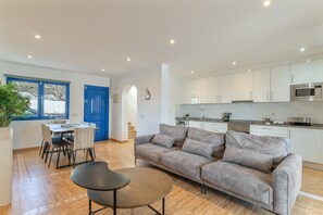 Een moderne keuken met witte kastjes, een grijze bank en een eethoek met een tafel en stoelen.