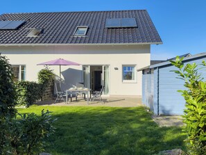 A house with a tiled roof, a patio with a table and chairs, and a small garden.