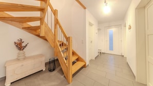 Unes escales de fusta condueixen a un segon pis, una paret blanca amb un vas decoratiu i un passadís amb una porta al final.