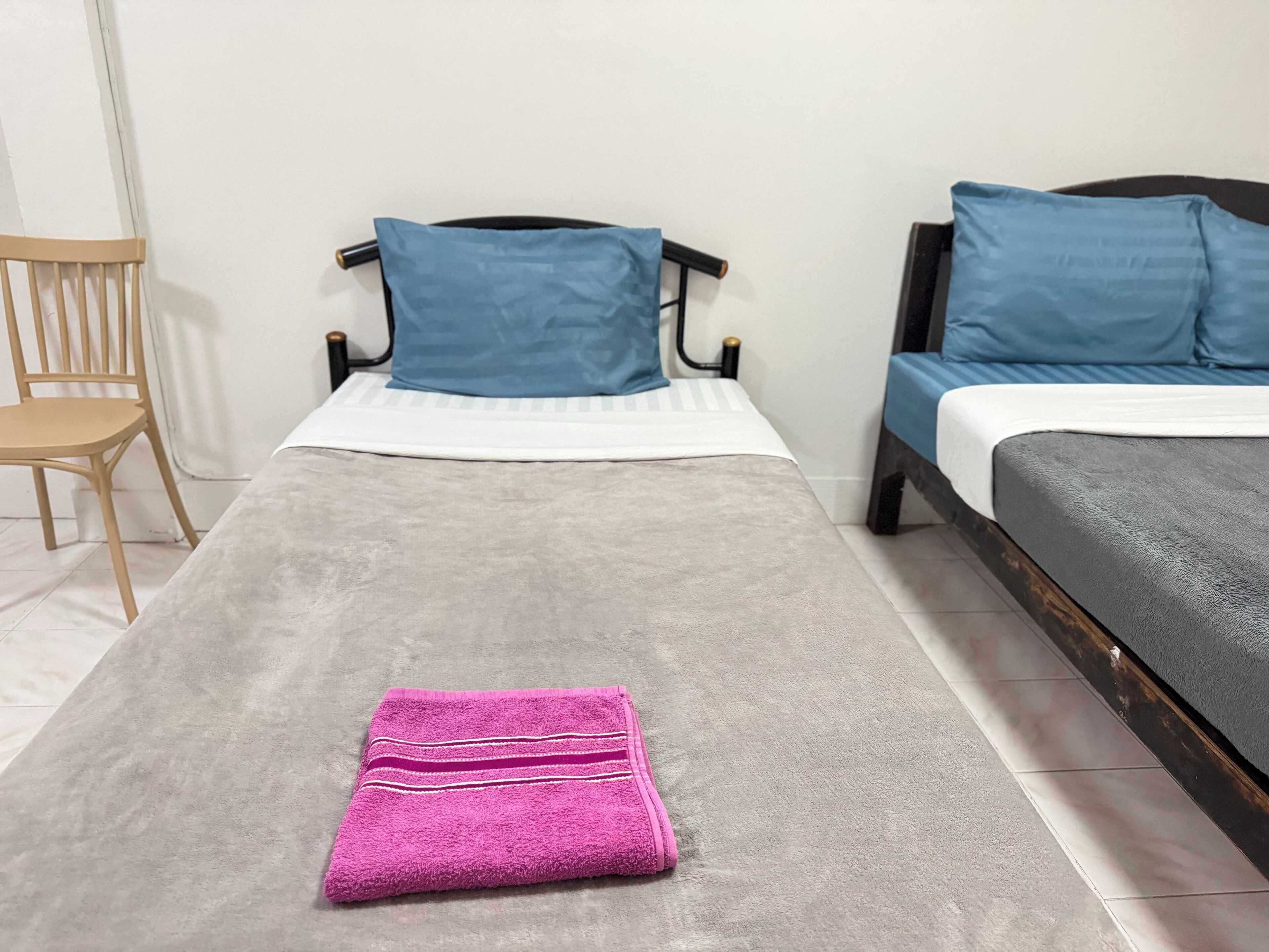 A room with two beds, a wooden chair, and a pink towel on the floor.