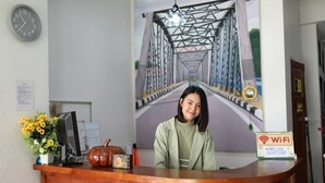 A reception desk with a clock, a Wi-Fi sign, a vase with flowers, and a painting of a bridge in the background. - Collection O Centre Place  (Chiang Mai)