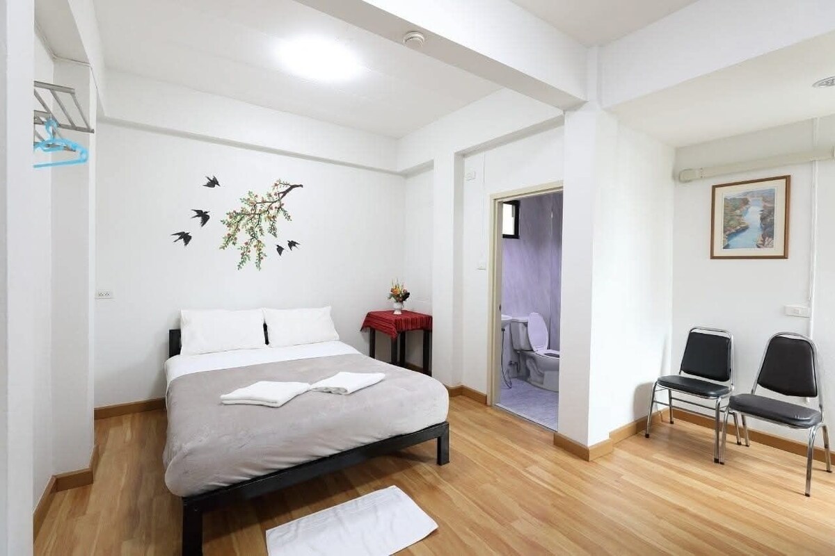 A modern hotel room with a bed, a small table with a vase, a chair, and a painting on the wall.