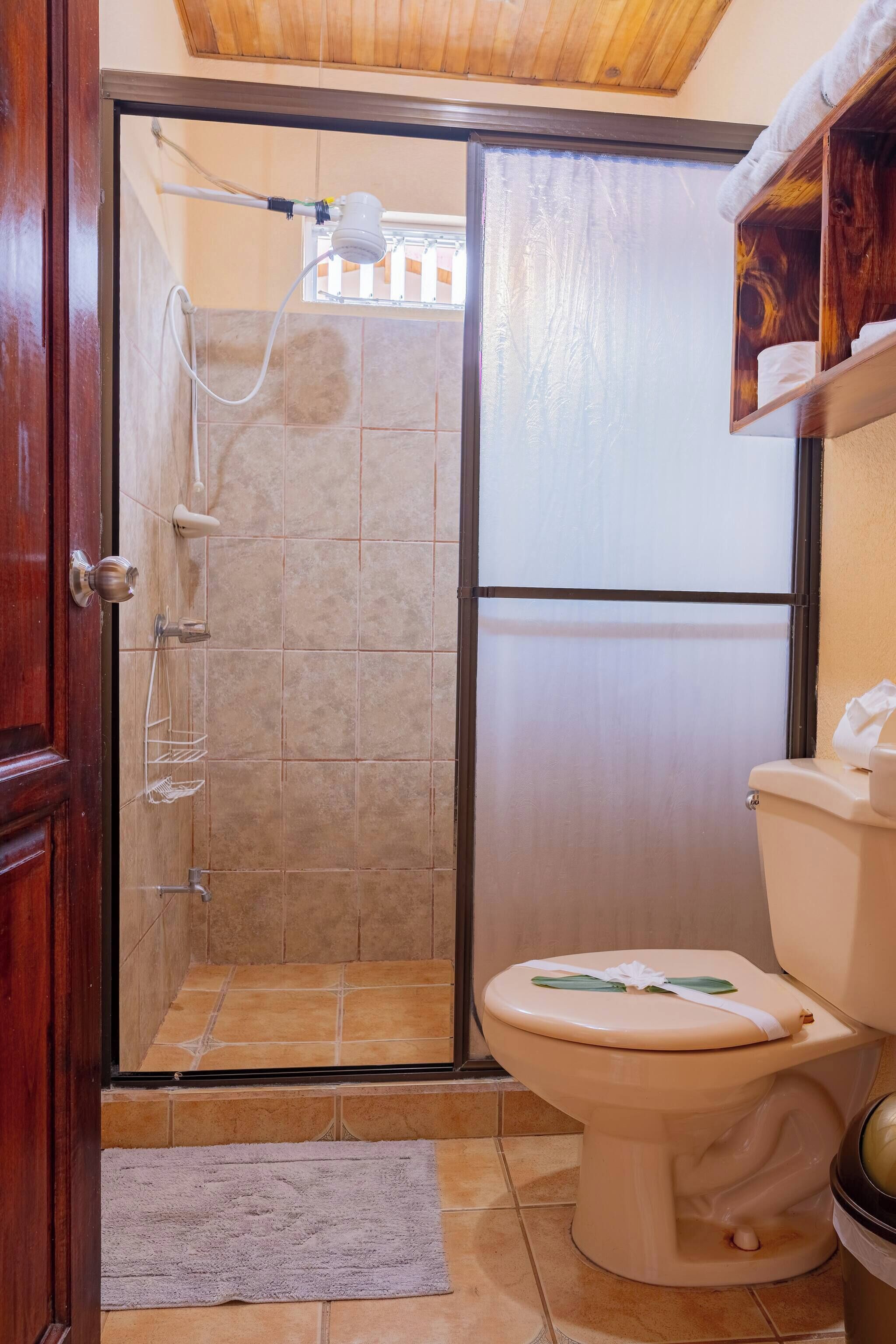 A bathroom with a shower, toilet, and a wooden shelf with towels.